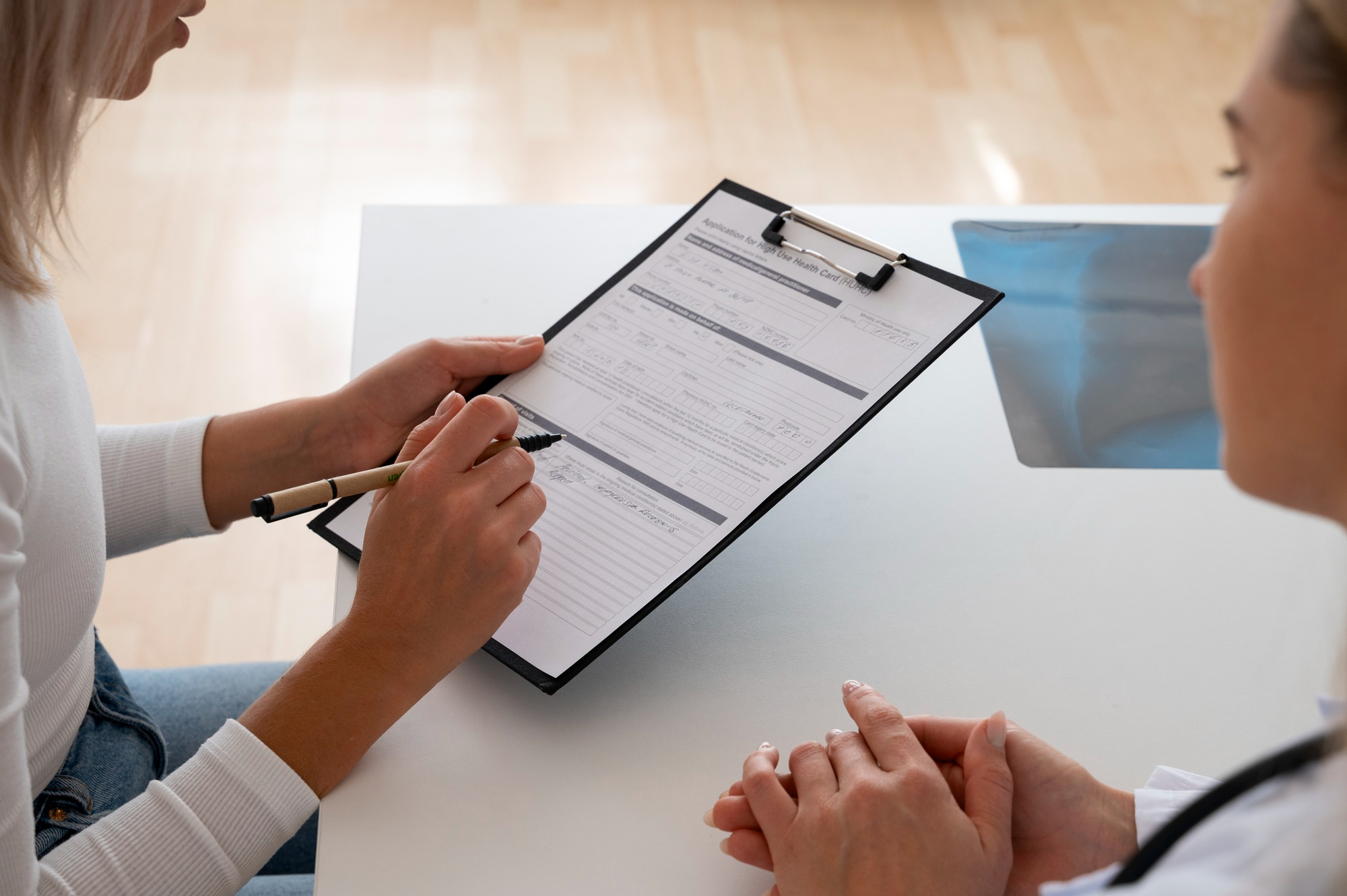 Close-up of patient filling medical form on clipboard during consultation.