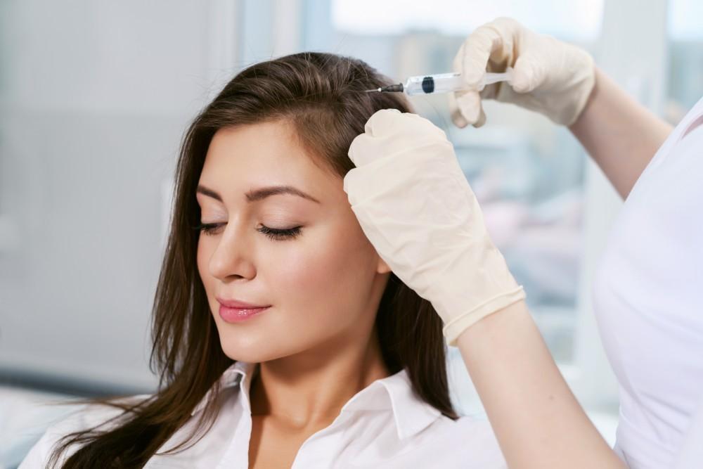 Young woman receiving scalp injection treatment for hair restoration.